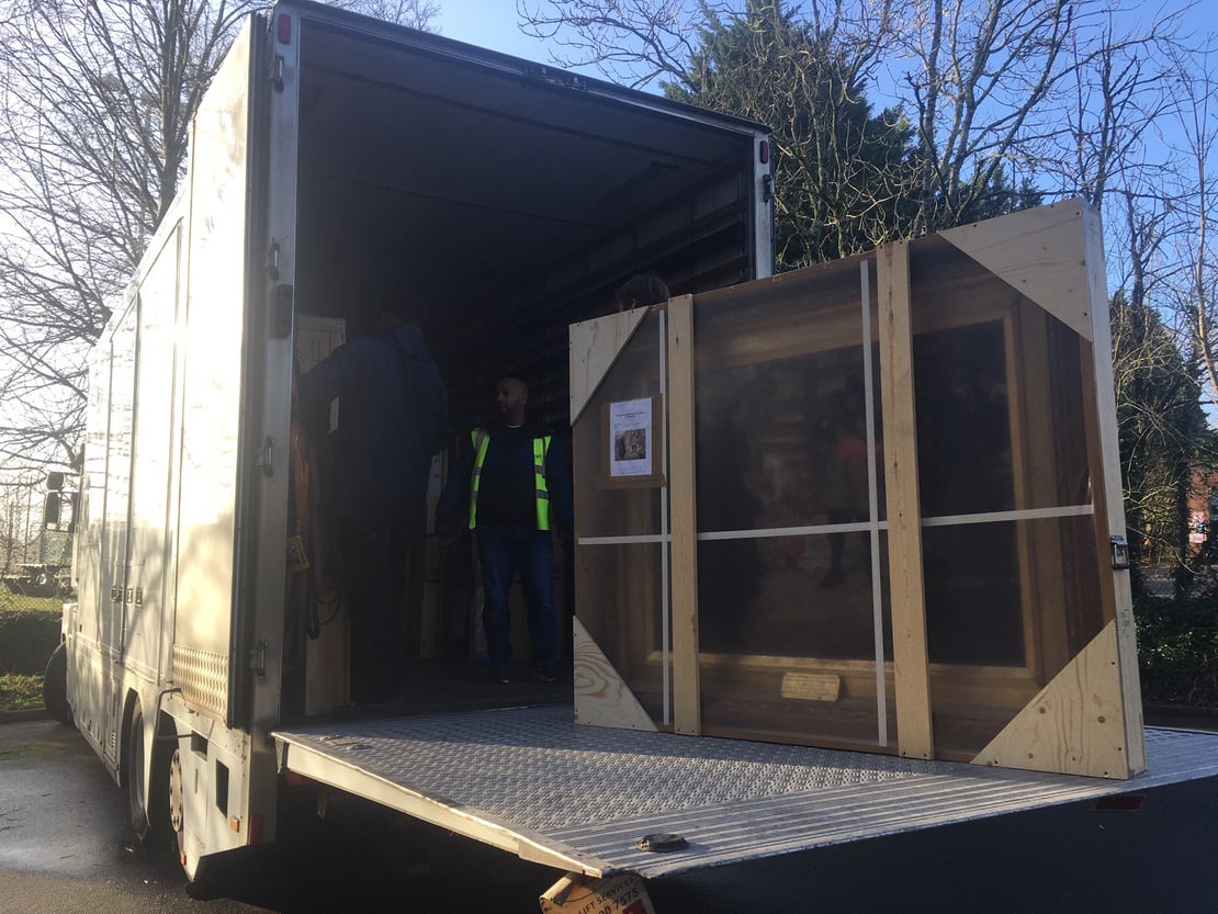 A large painting in a transit frame being loaded into a van