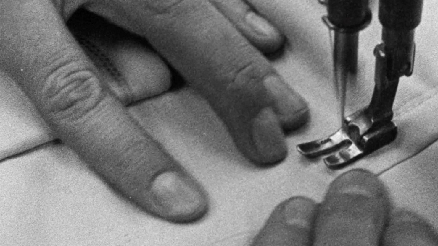 A black and white image showing a close up of someone's hands using a sewing machine