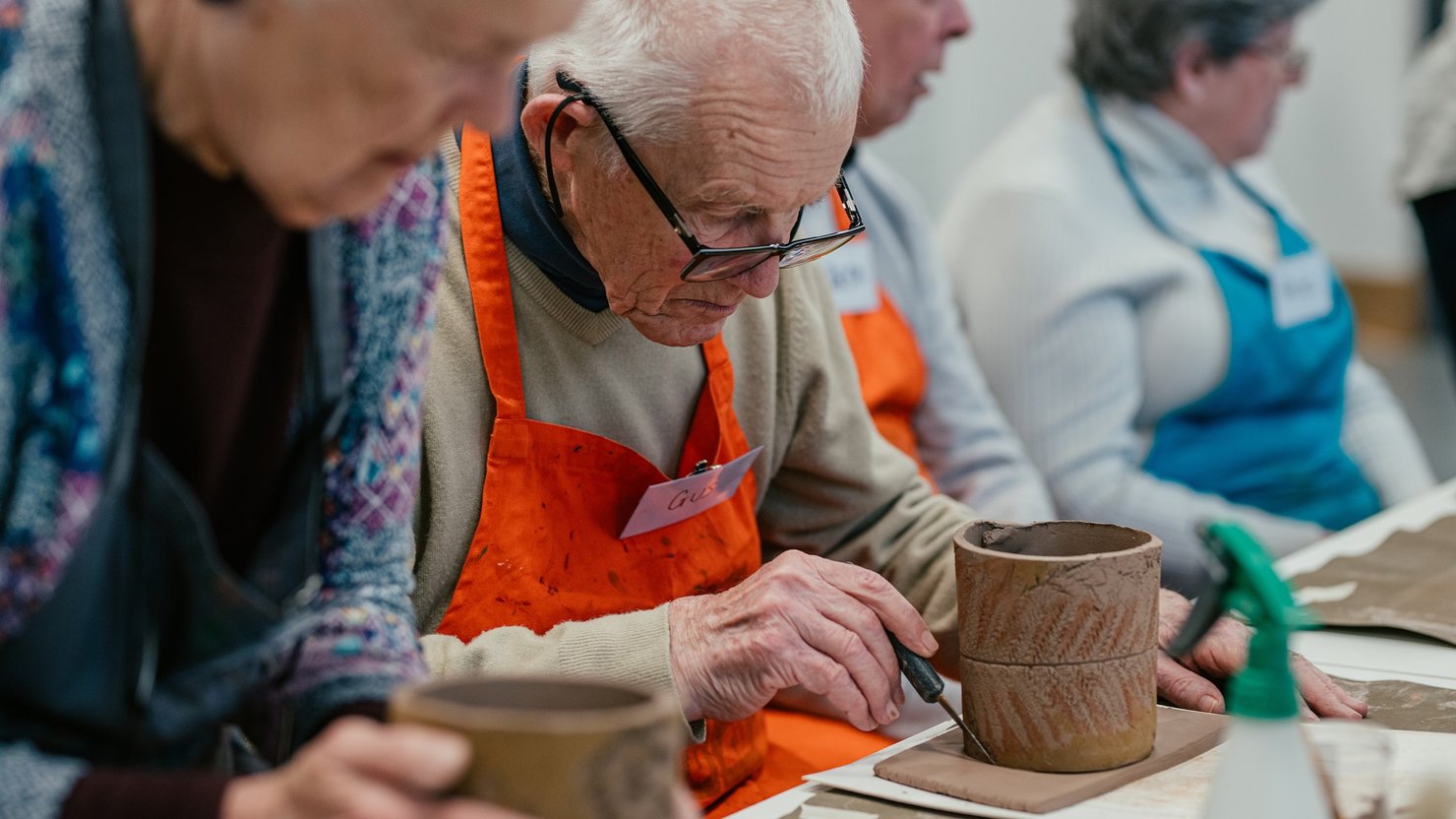 A photograph showing a man and a carer decorating a clay pot