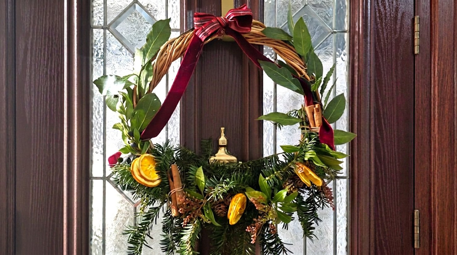 A festive wreath with ribbons and botanicals hanging on a brown door with glass panels