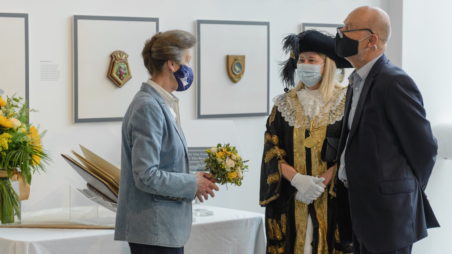 HRH Princess Anne talking to a man and a woman while holding a bunch of flowers