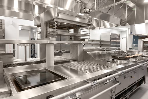 High-end commercial cooking line with stainless steel grill, griddle, range, overhead salamander broiler, and ventilation hood in a professional kitchen.