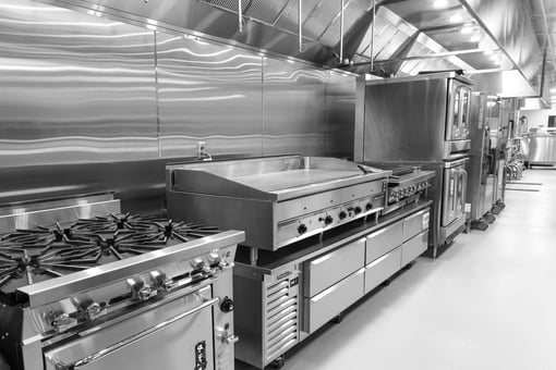Commercial kitchen cook line with gas range, flat-top griddle, convection ovens, refrigerated base drawers, and stainless steel ventilation hood.