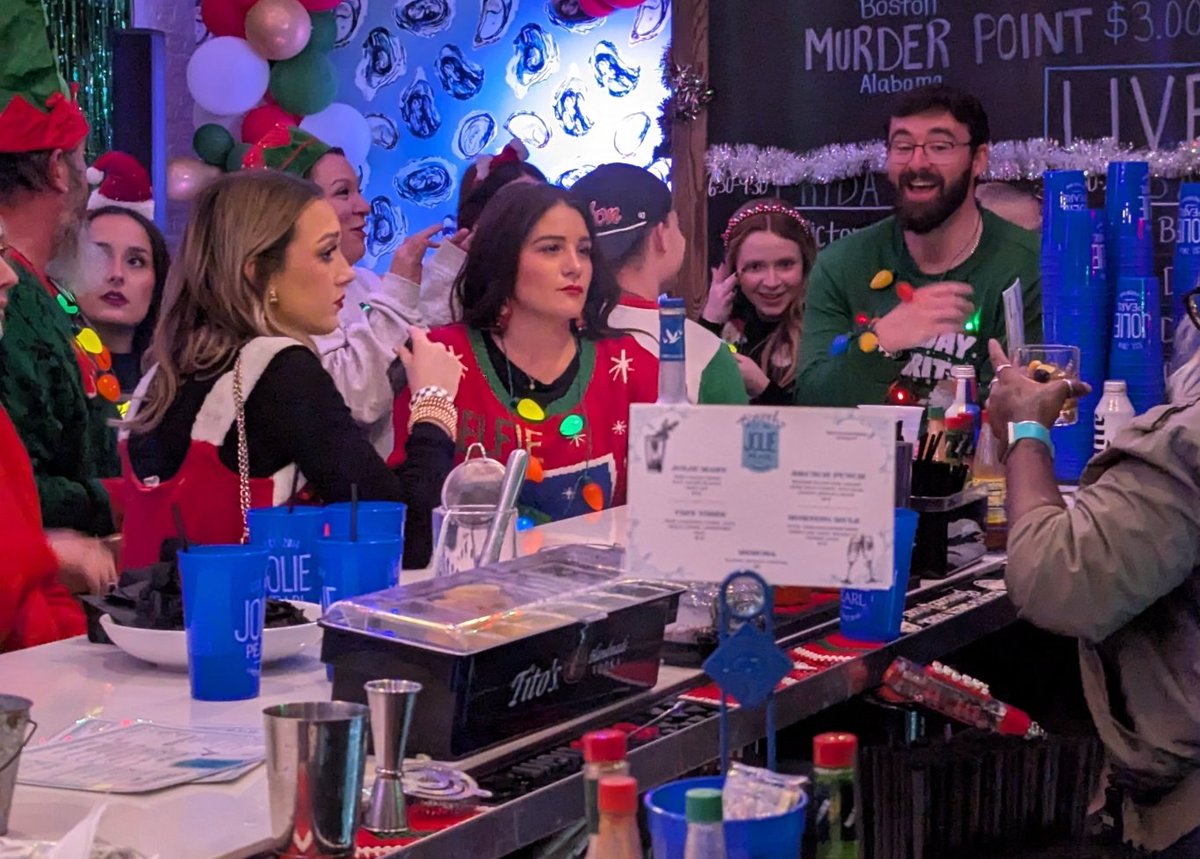 Bartenders in elf hats and light-up necklaces shake drinks behind a Jolie Pearl bar piled with blue souvenir cups