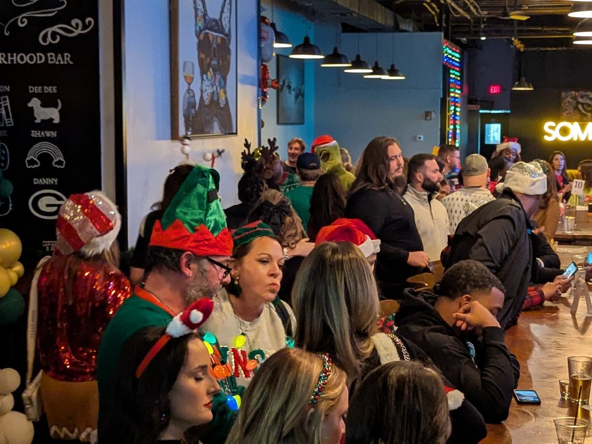 Packed bar crowd in elf hats, reindeer antlers and a Grinch mask elbow-up at the rail