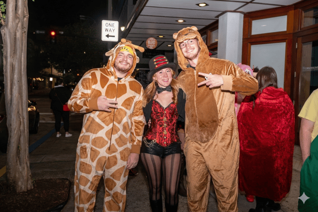 Giraffe and lion onesies flank a corseted devil on a sidewalk, costume crawl in full swing