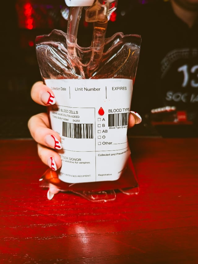Blood-dripped nails hold up an IV-style blood bag pouch on a dark bar top