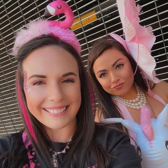 Selfie of two women in pink flamingo headband and feathered pink fascinator with pearl necklaces