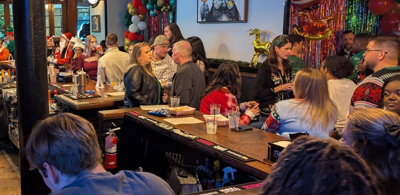 Ugly-sweater crowd packed shoulder-to-shoulder at a tinsel-trimmed bar