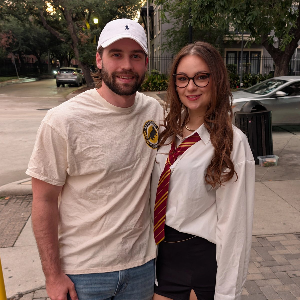 Witch in striped house tie and white shirt poses streetside with her muggle-welcome partner between wizard-crawl stops.