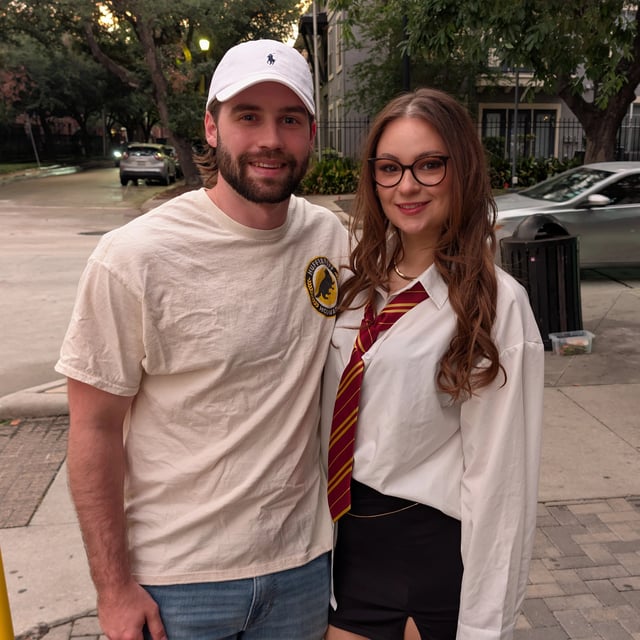 Witch in striped house tie and white shirt poses streetside with her muggle-welcome partner between wizard-crawl stops.