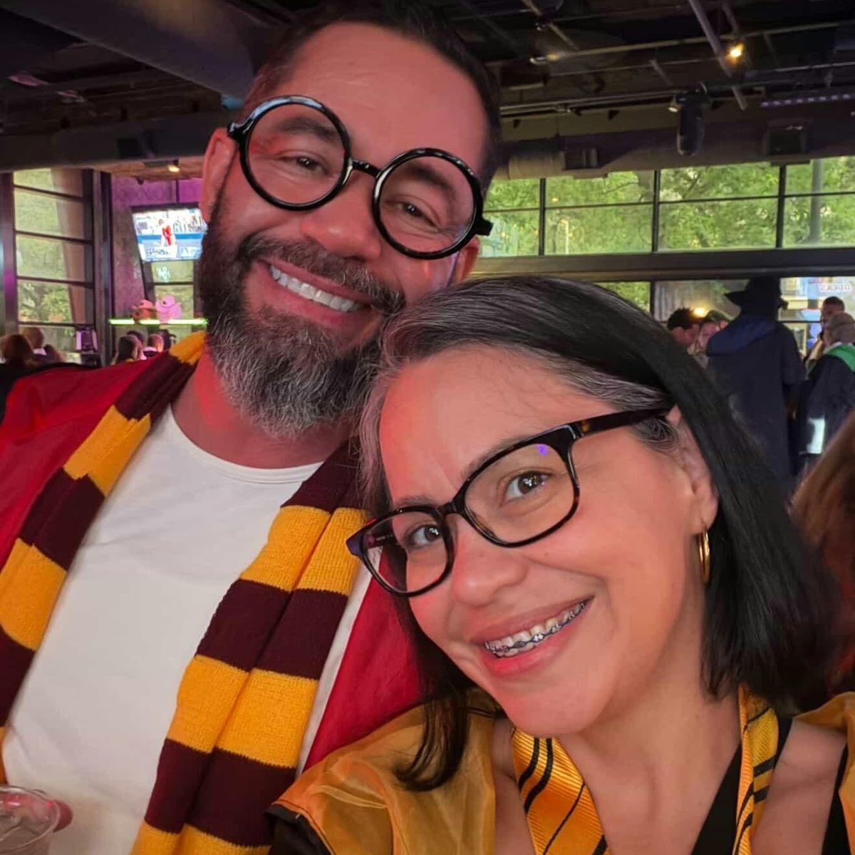 Wand-toting couple in round wizard specs and house scarves snap a spellbound selfie at a Wizards Night Out stop