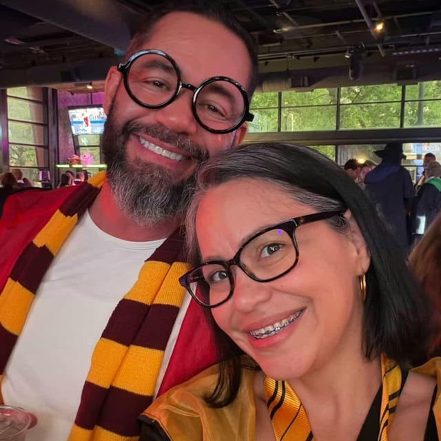 Wand-toting couple in round wizard specs and house scarves snap a spellbound selfie at a Wizards Night Out stop