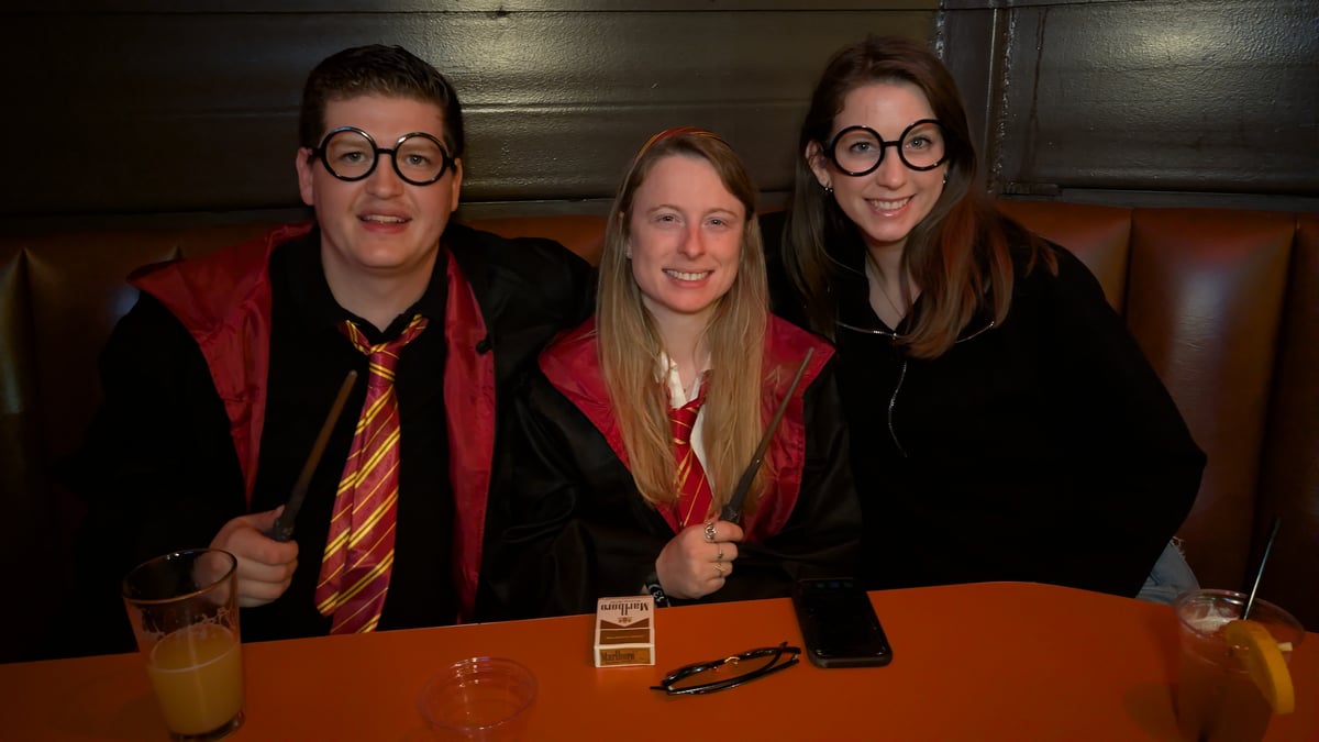 Three wand-wielding wizards in round Potter glasses, robes, and house ties hold court at a Wizards Night Out booth.