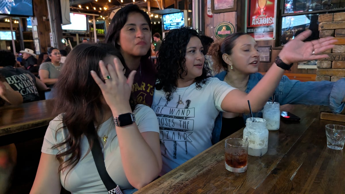 Witches laugh over butterbeer mugs on the wizard crawl, one wearing a Wand Chooses the Wizard tee