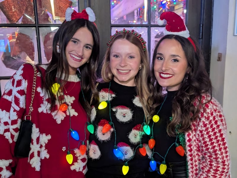 Three friends in matching ugly sweaters and glowing string-light necklaces
