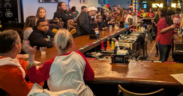 Bar lined with crawlers in Santa suits and sweaters, antler headbands glowing under festive lights