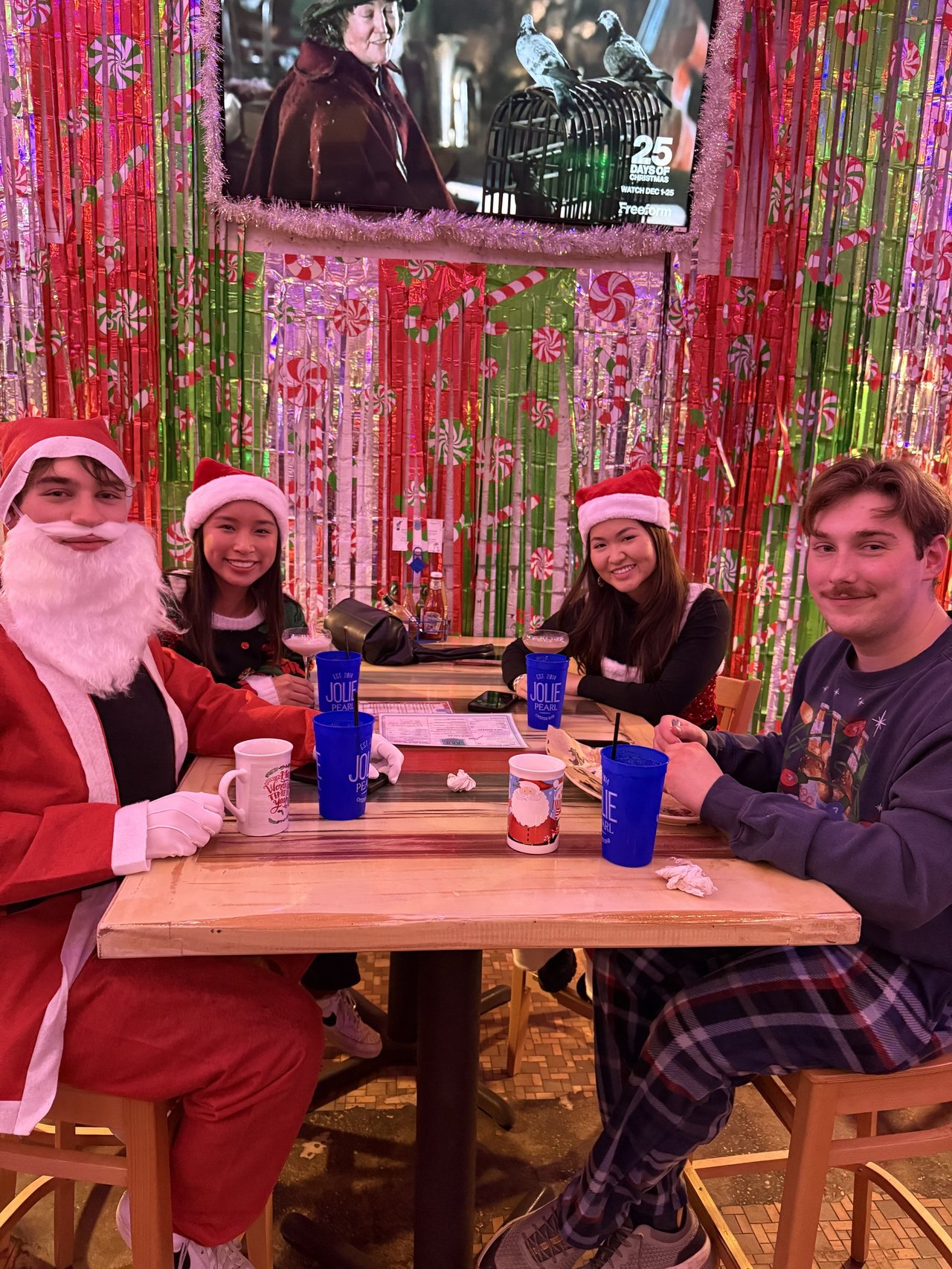 Four friends in Santa suits and Christmas sweaters at a bar decked out in red and green candy-cane tinsel — Bad Santa Pub Crawl, Austin