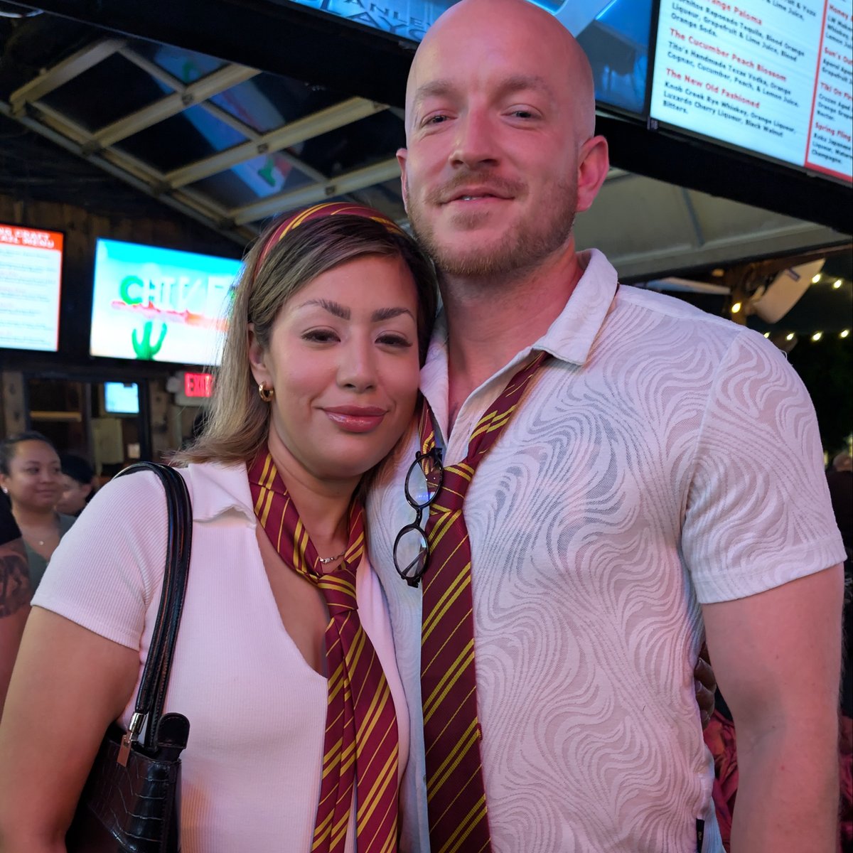 Wizards Night Out couple in matching Gryffindor ties and round specs snuggle close at a sports bar stop
