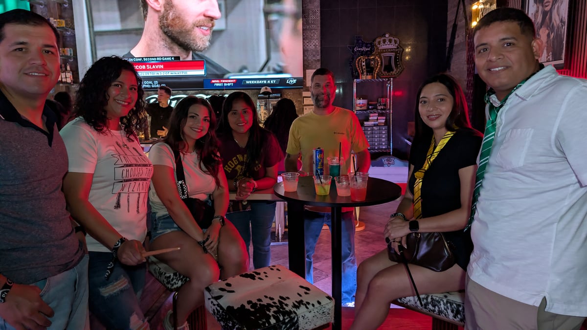 Wizards Night Out crew in Hogwarts tees, ties, and a Slytherin scarf gather around a booth with wands and potion glasses in hand.