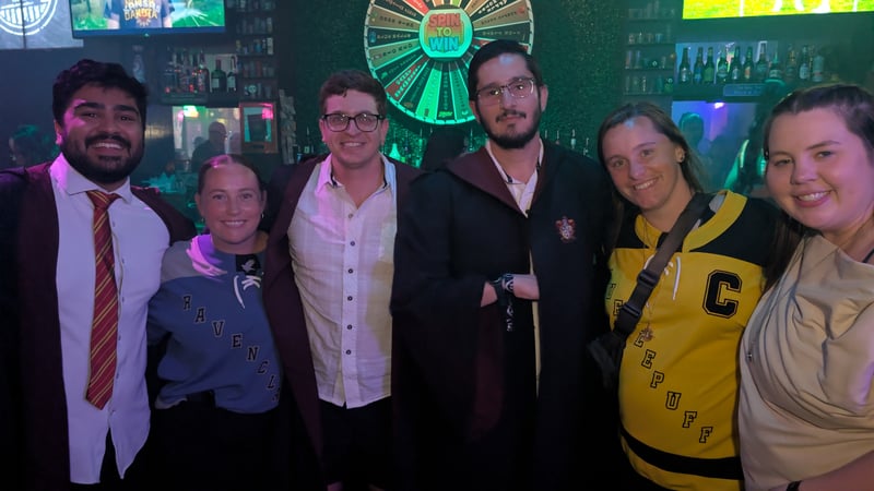 Seven house-gear-clad wizards line up beside a Spin to Win wheel on the crawl