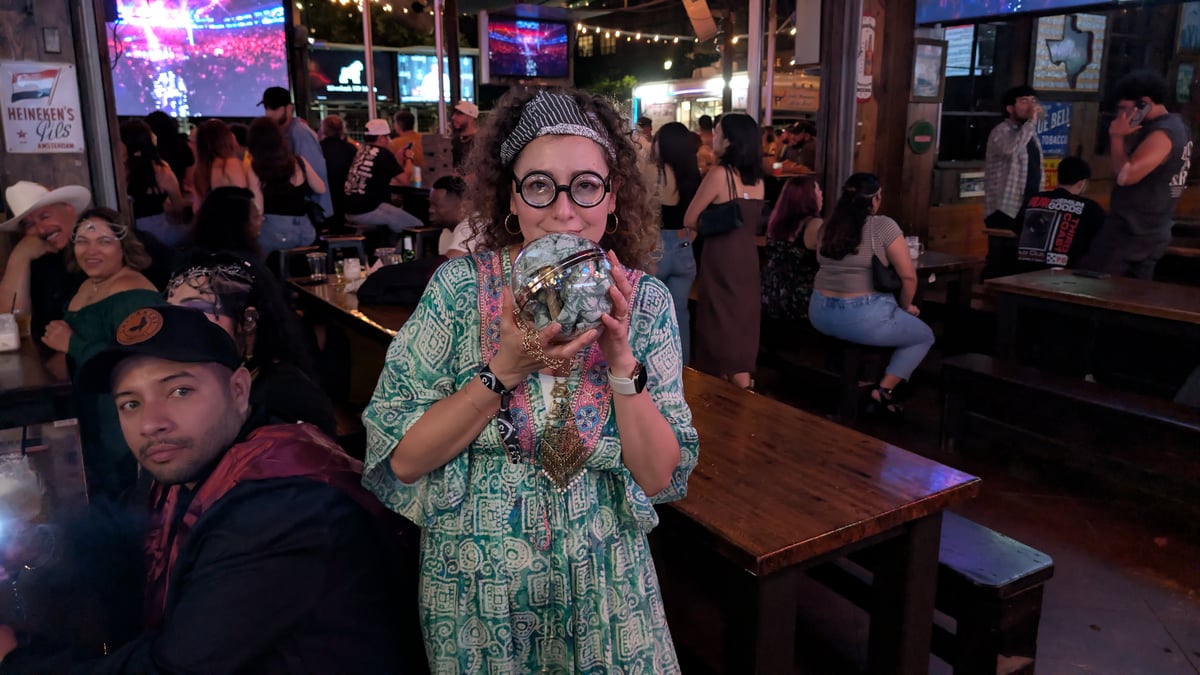Birthday witch in round specs and headband cradles a crystal-ball potion glass at a Wizards Night Out stop