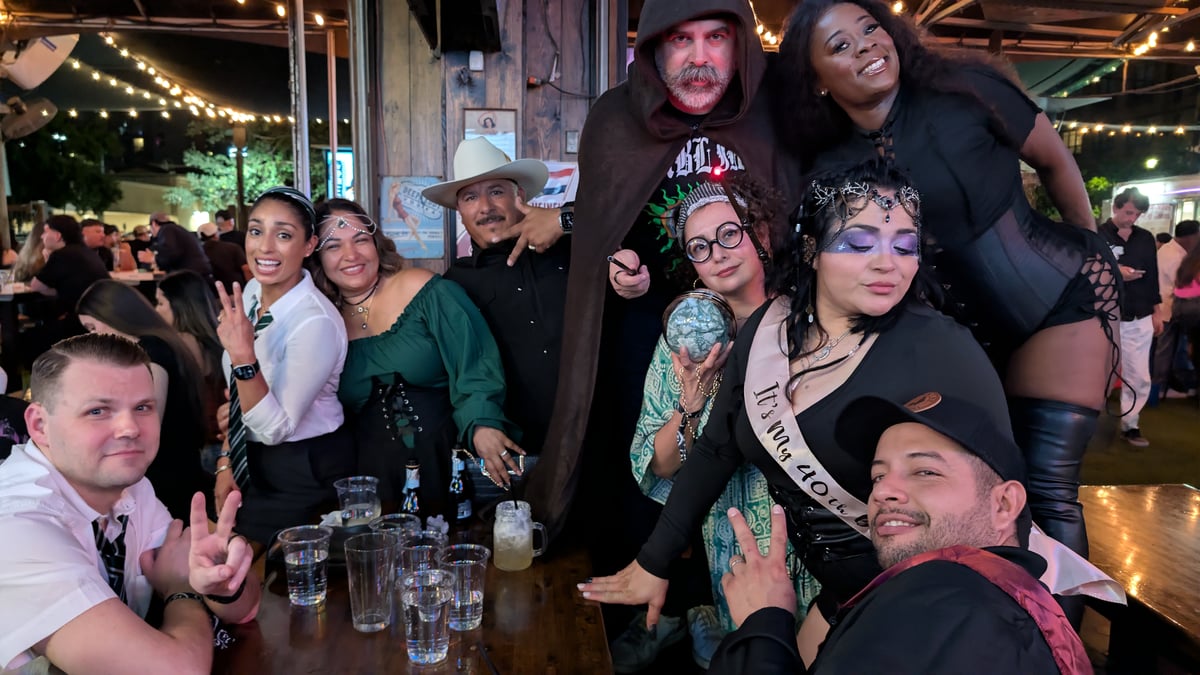 Wide shot of a birthday Wizards Night Out crew with hooded sorcerer, crystal ball and house-tie sashes at the bar