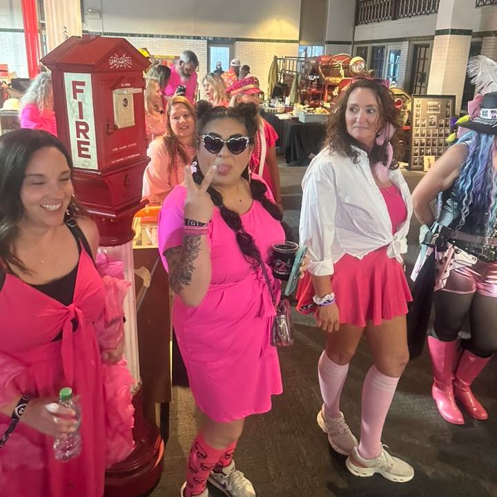 Crawlers in hot pink dresses and wigs strike poses beside an antique fire alarm box