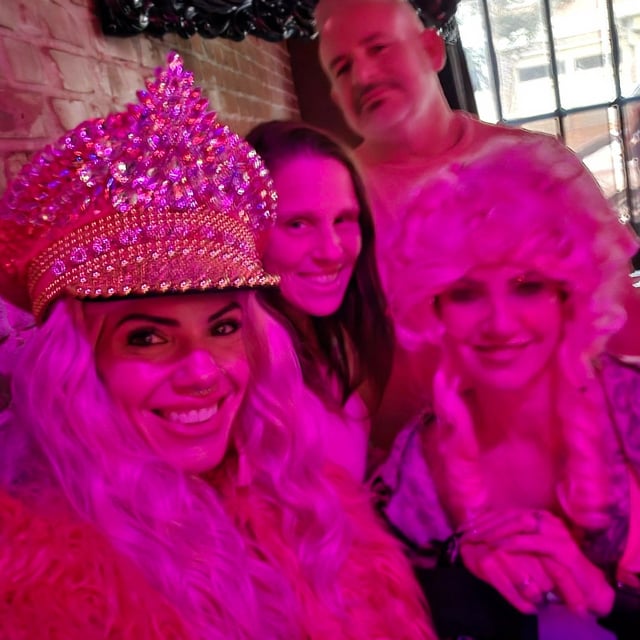 Pink-lit bar selfie of friends in blonde wigs and a sparkly pink jeweled captain hat