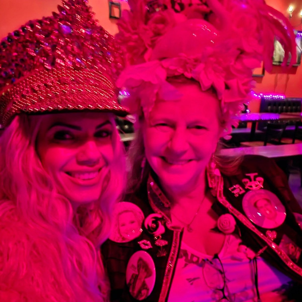 Selfie under pink lighting of two crawlers in jeweled pink hats and button-covered jacket