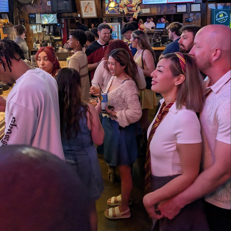 Crowded wizard crawl stop with house-tie-clad witches and wizards mingling between butterbeers