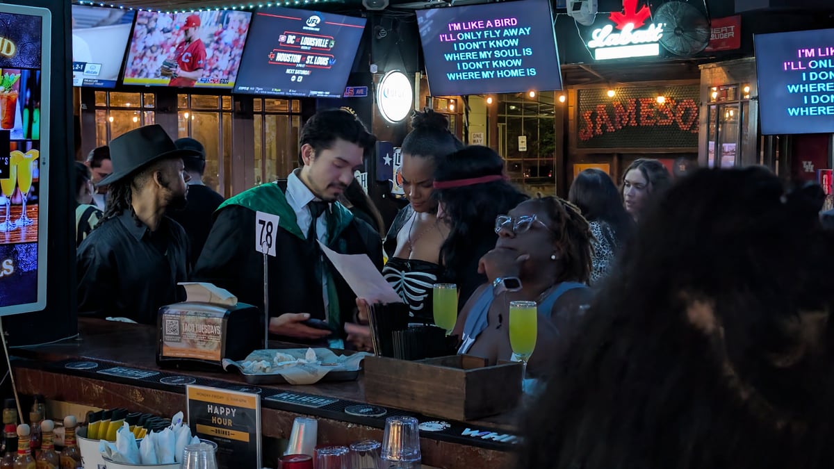 Robed wizards order butterbeer-style drinks at a karaoke bar stop, lyrics flashing on the screens above