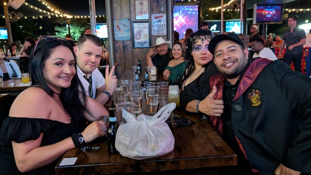 Thumbs-up Wizards Night Out crew in Gryffindor robes and crystal-ball headpieces toast at an empty-glass patio table