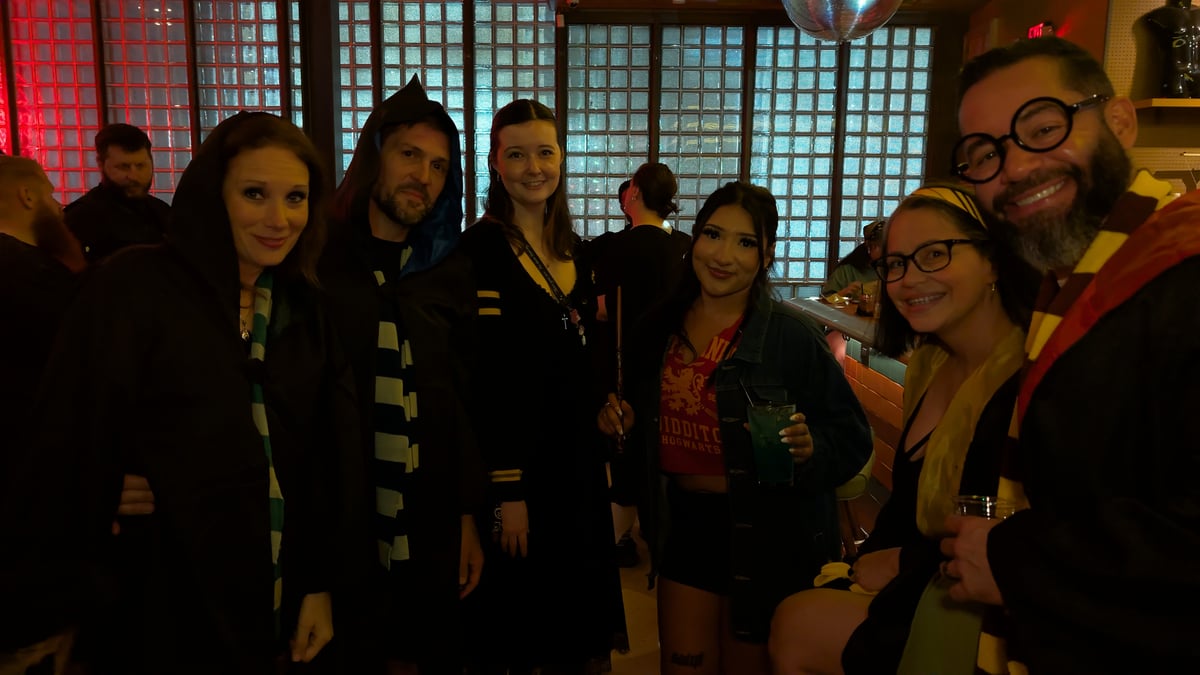 Hooded wizards-in-training in Quidditch tee, house scarves, and round Potter glasses gather at a glass-brick crawl stop.