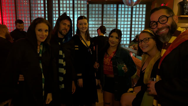 Hooded wizards-in-training in Quidditch tee, house scarves, and round Potter glasses gather at a glass-brick crawl stop.