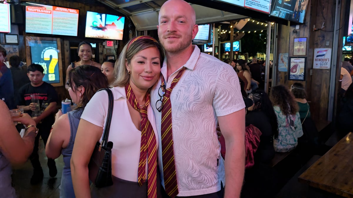 Gryffindor-tied couple with round specs tucked into a collar pose at a string-lit patio Wizards Night Out stop