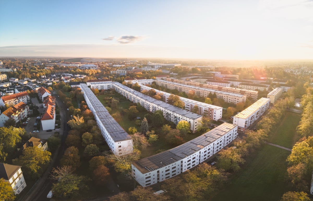 Aerial view of a residential area with long apartment blocks whose roofs are covered with photovoltaic modules.
