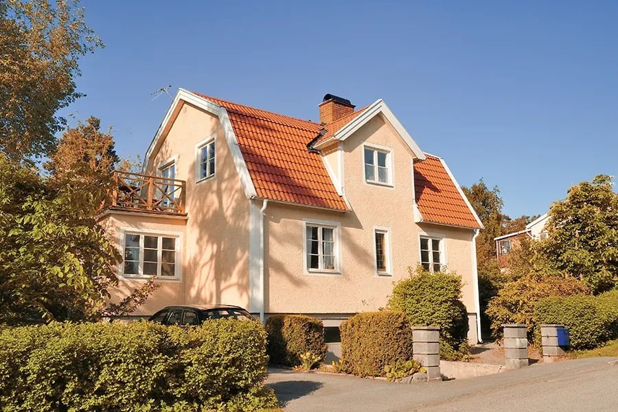 Two-storey rendered house with a red tiled pitched roof, a dormer and a brick chimney, with a clipped hedge in front.