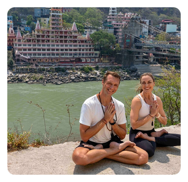 Taryn and Yann seated in lotus beside the Ganges in Rishikesh, India