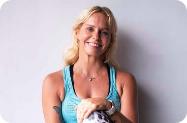 Smiling Loka Yoga School instructor in a blue top seated against a plain wall