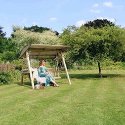 Relaxing outdoor garden swing with lush greenery in a spacious backyard, ideal for outdoor living and enhancing home garden aesthetics.