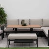 Modern outdoor patio furniture with beige cushions, black metal frames, and wooden accents, surrounded by lush flowering plants and artificial grass, perfect for garden lounging and entertaining.