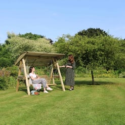 Relaxing garden swing with women enjoying outdoor leisure in a lush green backyard.