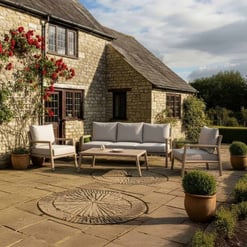 Cozy outdoor patio with white cushioned furniture and potted plants in front of a rustic stone cottage, perfect for garden entertaining and relaxation.