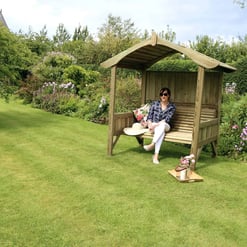 Rustic wooden garden shelter with seating, ideal for outdoor relaxing and enjoying nature, surrounded by lush greenery and blooming flowers. Perfect addition to home garden or outdoor space.