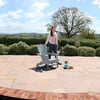 Adirondack-style garden chair on a patio with a woman standing nearby, enjoying a peaceful outdoor space with lush greenery and scenic rolling hills, perfect for outdoor living and relaxation.
