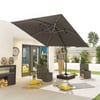 Large outdoor beige patio with a woman adjusting a large black patio umbrella, featuring patio furniture, potted plants, decorative pillows, and modern garden design, perfect for outdoor entertainment and relaxation.
