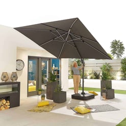 Large outdoor beige patio with a woman adjusting a large black patio umbrella, featuring patio furniture, potted plants, decorative pillows, and modern garden design, perfect for outdoor entertainment and relaxation.