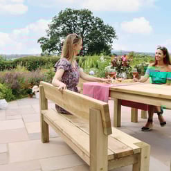 Beautiful outdoor dining scene with two women enjoying a meal on a wooden patio table surrounded by lush garden in summer. Perfect for garden furniture, outdoor dining, and patio decor inspiration.