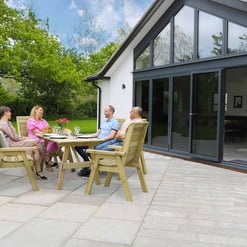 Elegant outdoor dining area with wooden furniture, large sliding glass doors, and lush green garden backdrop, perfect for entertaining in a modern home.